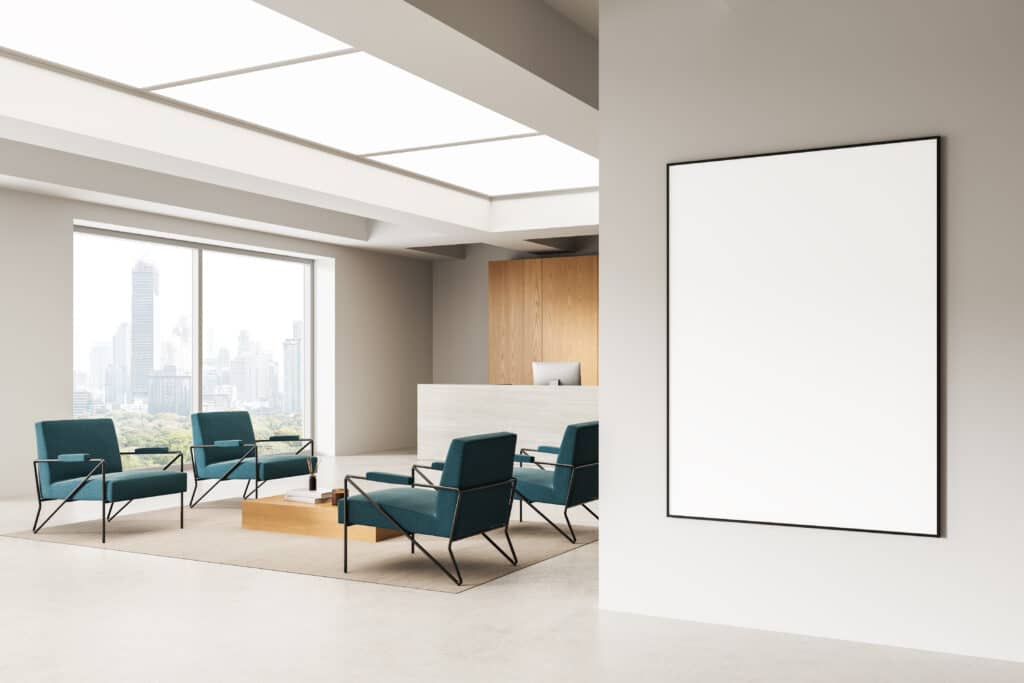 Bureau d'accueil moderne avec fauteuils turquoise, grande baie vitrée vue ville, et cadre blanc vide sur mur beige.