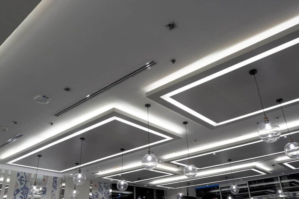 Plafond moderne avec éclairage indirect à LED formant des rectangles lumineux et suspensions à ampoules sphériques en verre.