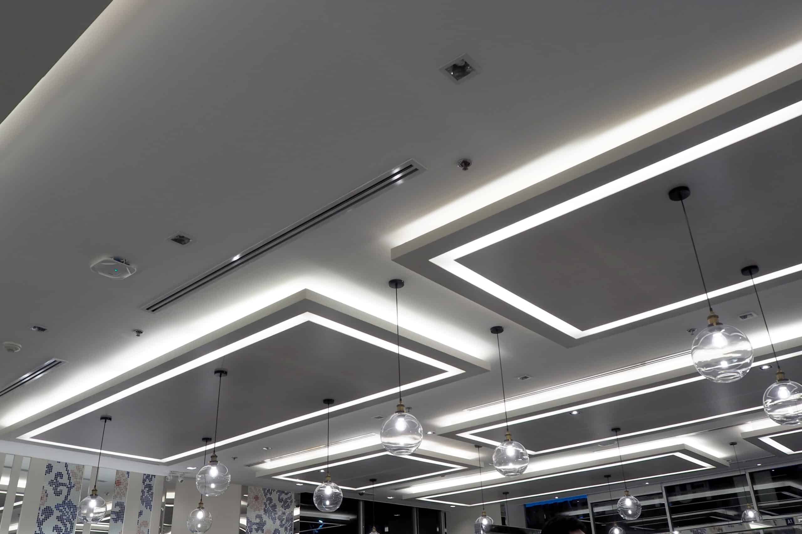 Plafond moderne avec éclairage indirect à LED formant des rectangles lumineux et suspensions à ampoules sphériques en verre.