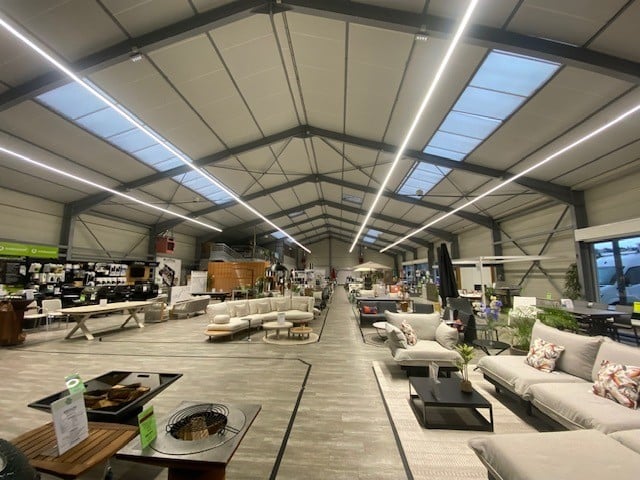 Showroom de mobilier de jardin : canapés et tables sous un toit industriel lumineux.