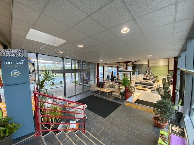 Showroom Fermob 100% Outdoor avec mobilier de jardin, canapés et plantes vertes vus depuis un escalier.