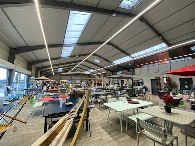 Showroom de mobilier de jardin avec tables colorées et parasols dans un grand espace industriel lumineux.