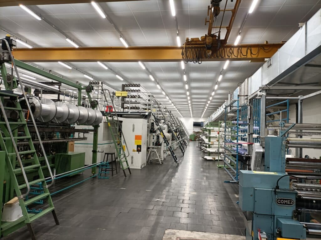 Atelier de Tissage : Machines Karl Mayer et Comez Usine textile avec métiers à tisser Karl Mayer, Comez et pont roulant industriel.